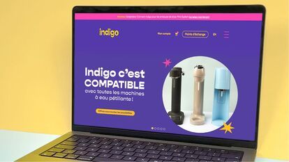 Un ordinateur portable affiche une page web promotionnelle pour un adaptateur de machine à eau pétillante de marque Indigo. L'adaptateur est compatible avec toutes les marques de machines à eau pétillante. Trois machines à eau pétillante de différentes co