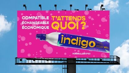 A bright pink billboard with the text “Compatible, Exchangeable, Economical. What are you waiting for?” in large white letters. In the center of the image, a cylinder of Indigo C02 is highlighted, with the words “indigo” and “Vos bulles d'ici” (“Your bubb