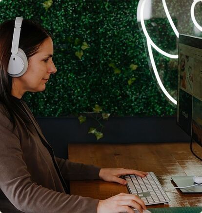 Une designer graphique, casque audio sur les oreilles, est absorbée par un projet créatif. Elle est assise à son espace de travail sur la Rive-Nord de Montréal, élaborant l'image de marque d'un client de l'agence marketing. 