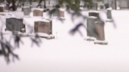 Pierres tombales recouvertes de neige dans un cimetière en hiver. Des branches d'arbre enneigées sont floues au premier plan.