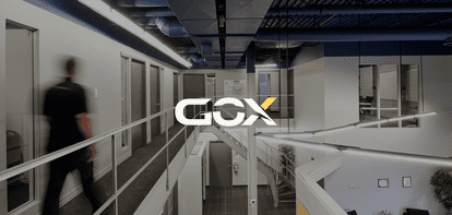 Un homme flou marche dans un couloir de bureau avec le logo GOX au premier plan.